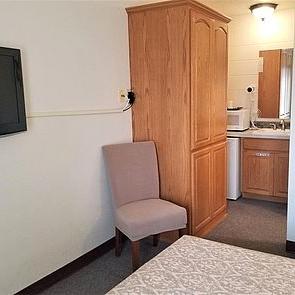 Guestroom armoire, chair, microwave, refrigerator, and sink area